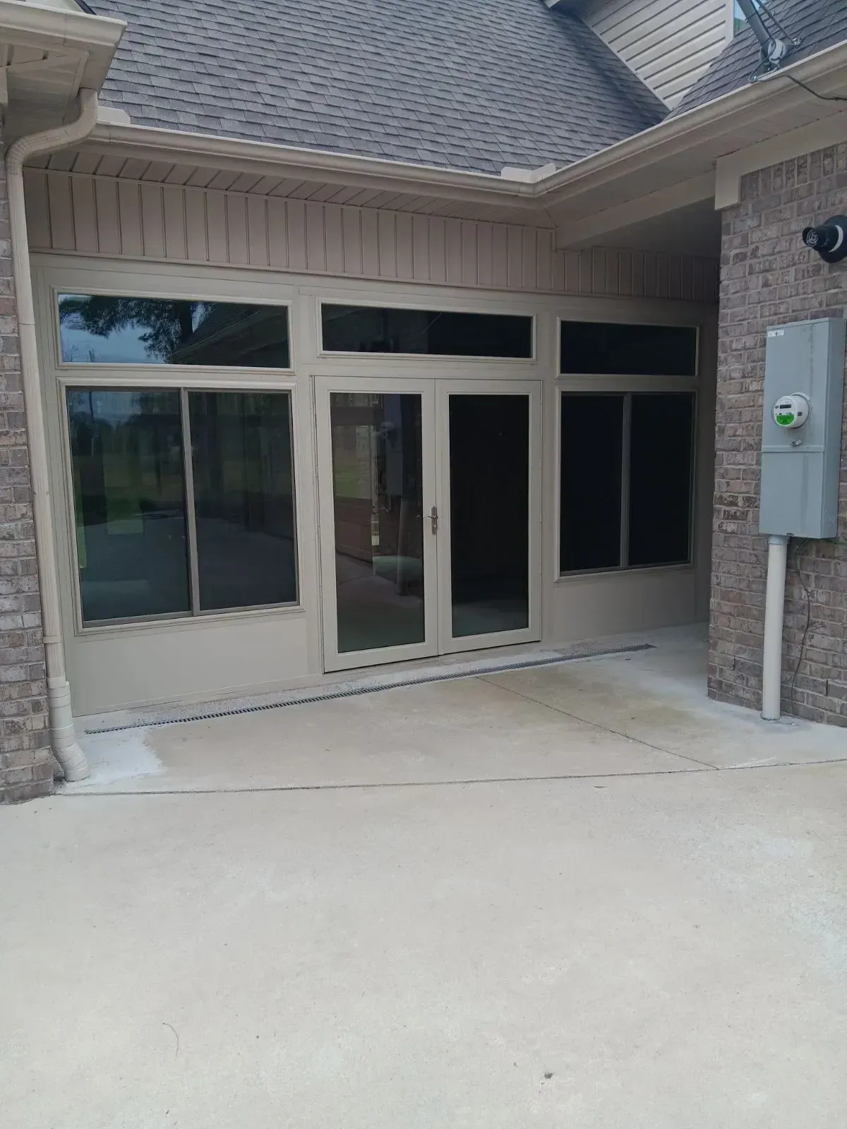 Covered patio entrance with glass doors and windows, beige stucco walls, and a concrete walkway