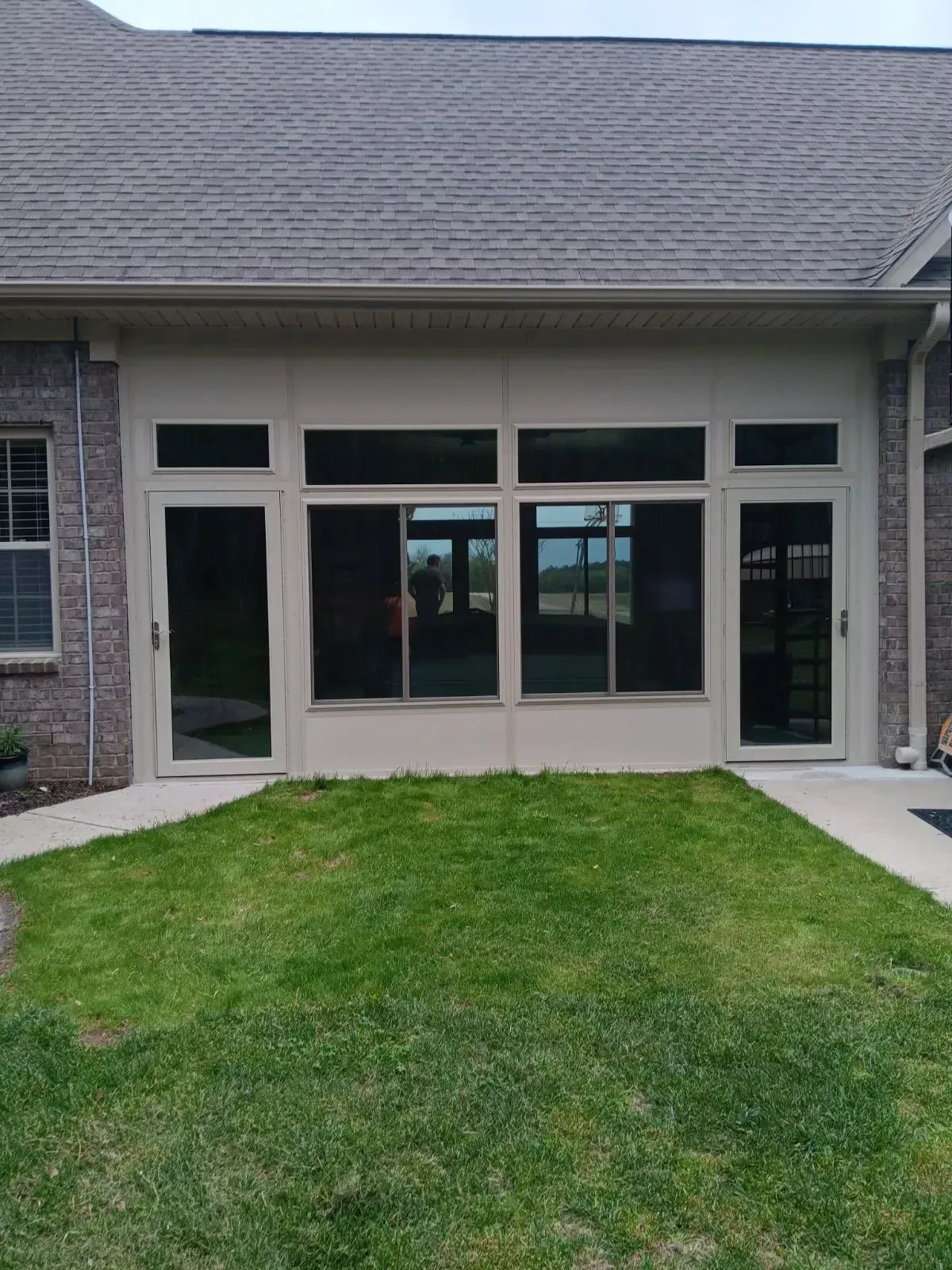 Covered patio with screened windows and doors behind a small grassy yard.