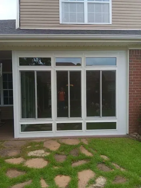 Front of a house with large white-framed windows and a brick wall above a stone path and lawn