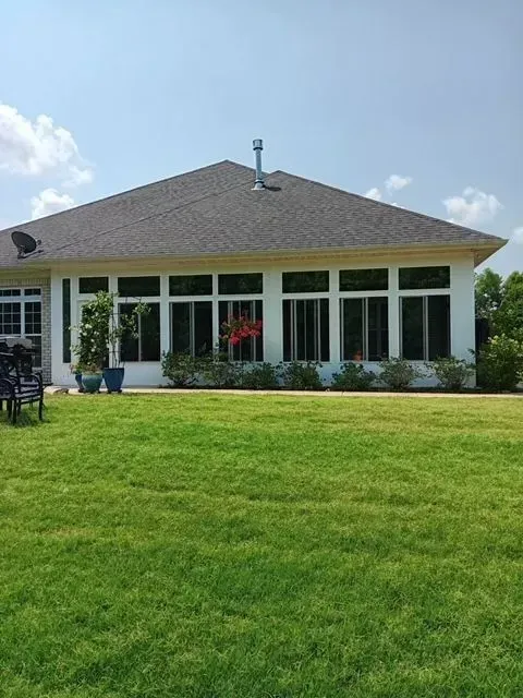 Single-story house with a gray roof, white columns, and a lush green lawn under a blue sky