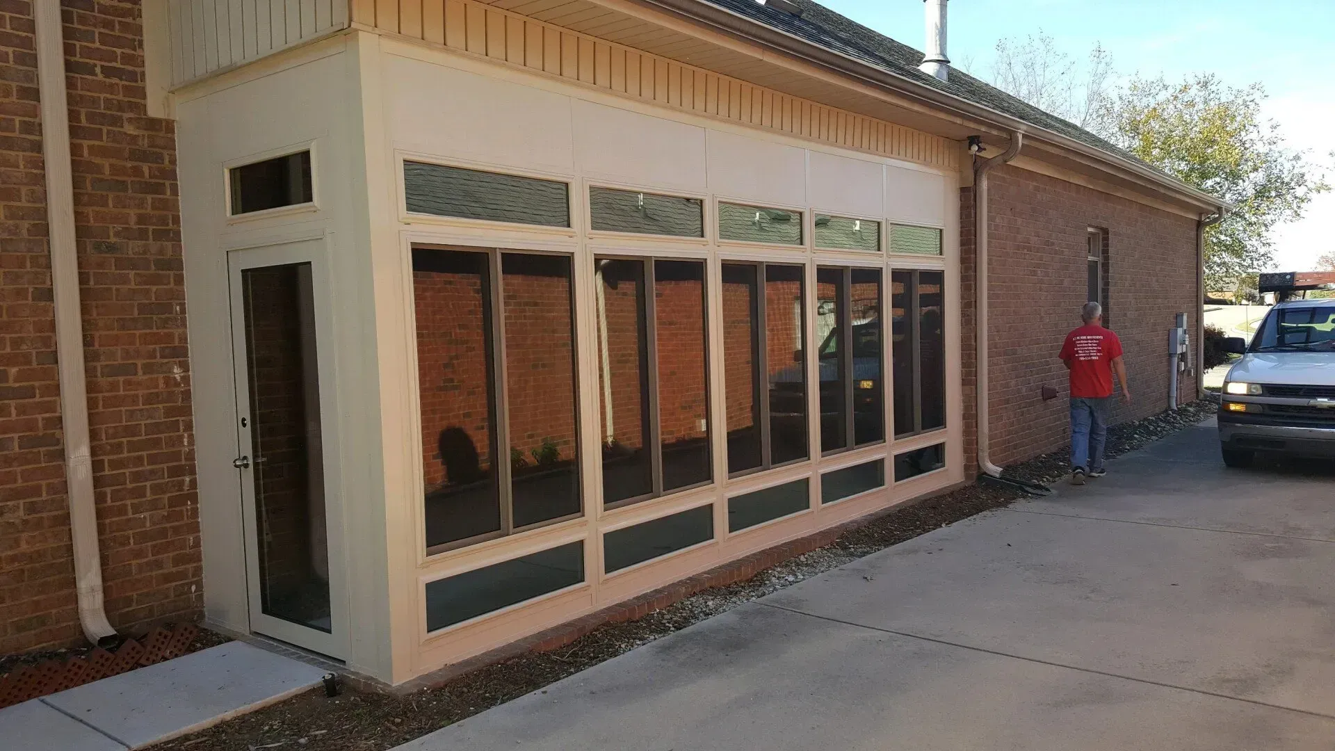 Brick building with large windows, a person in a red jacket near the wall, and a parked truck at the driveway.