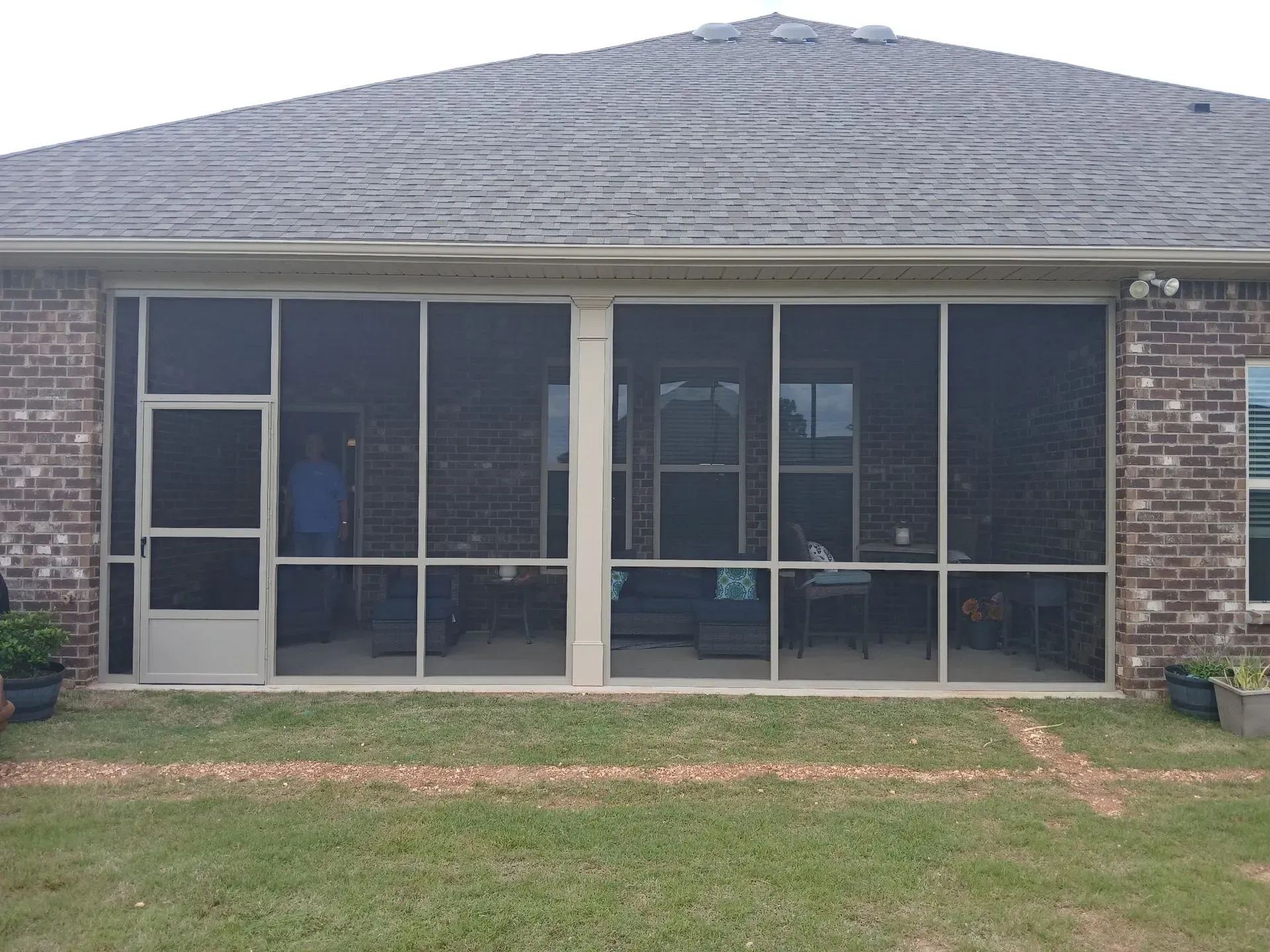 Brick house screened porch with white-framed windows and a gray shingled roof.