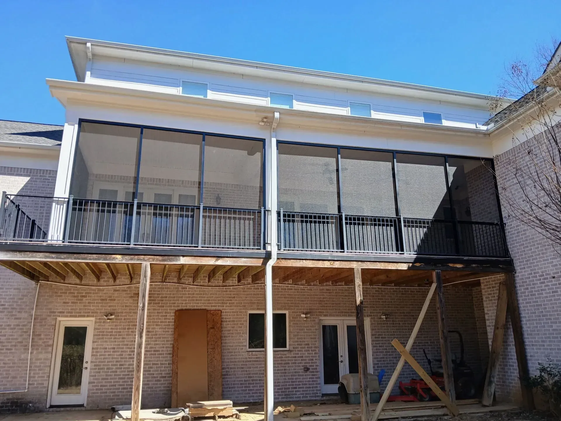 Backyard view of a two-story brick house with screened upper porch and white trim under a blue sky