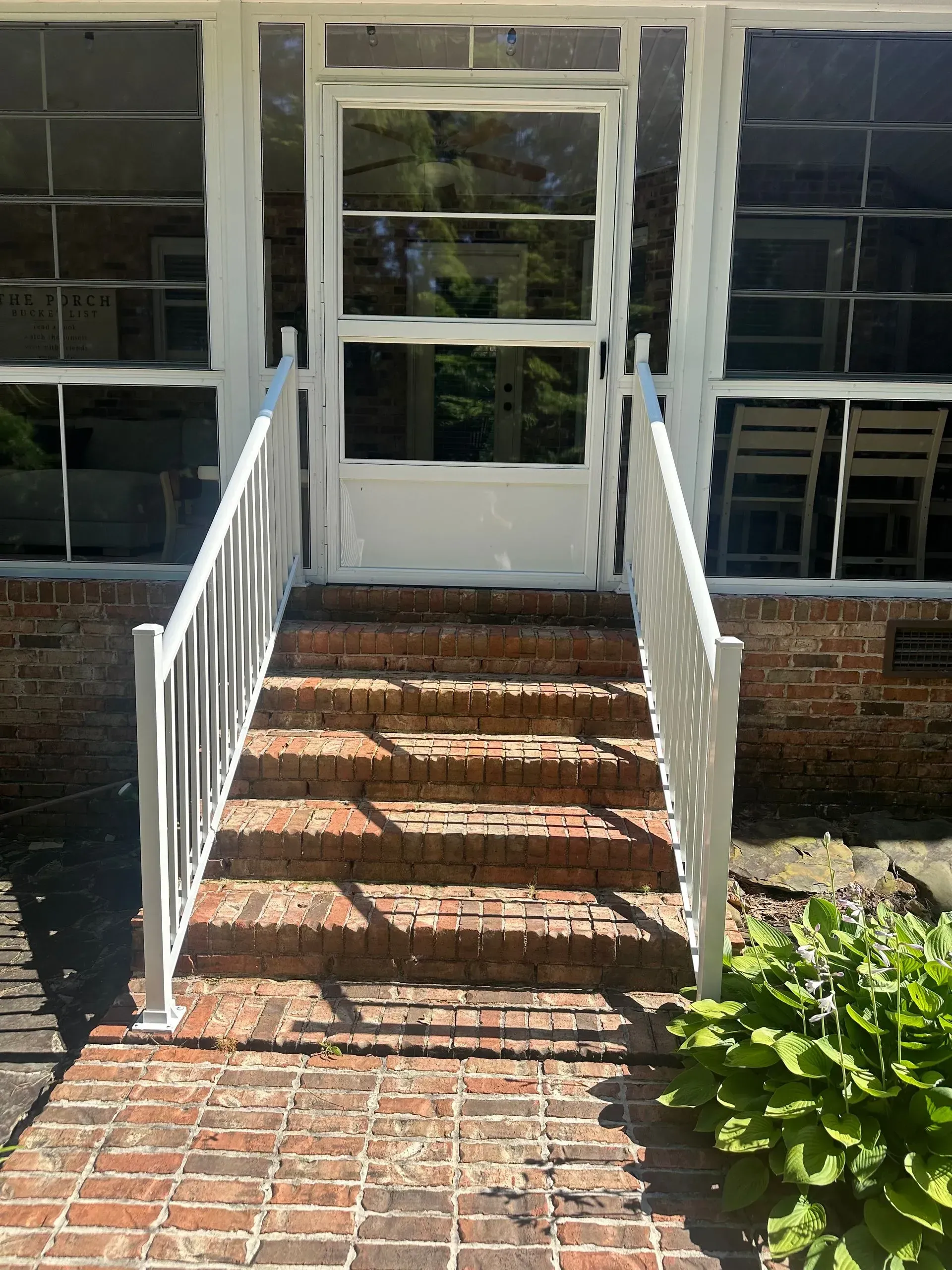 Front steps with white railings leading to a white door on a brick house, with a sunny shadow pattern.