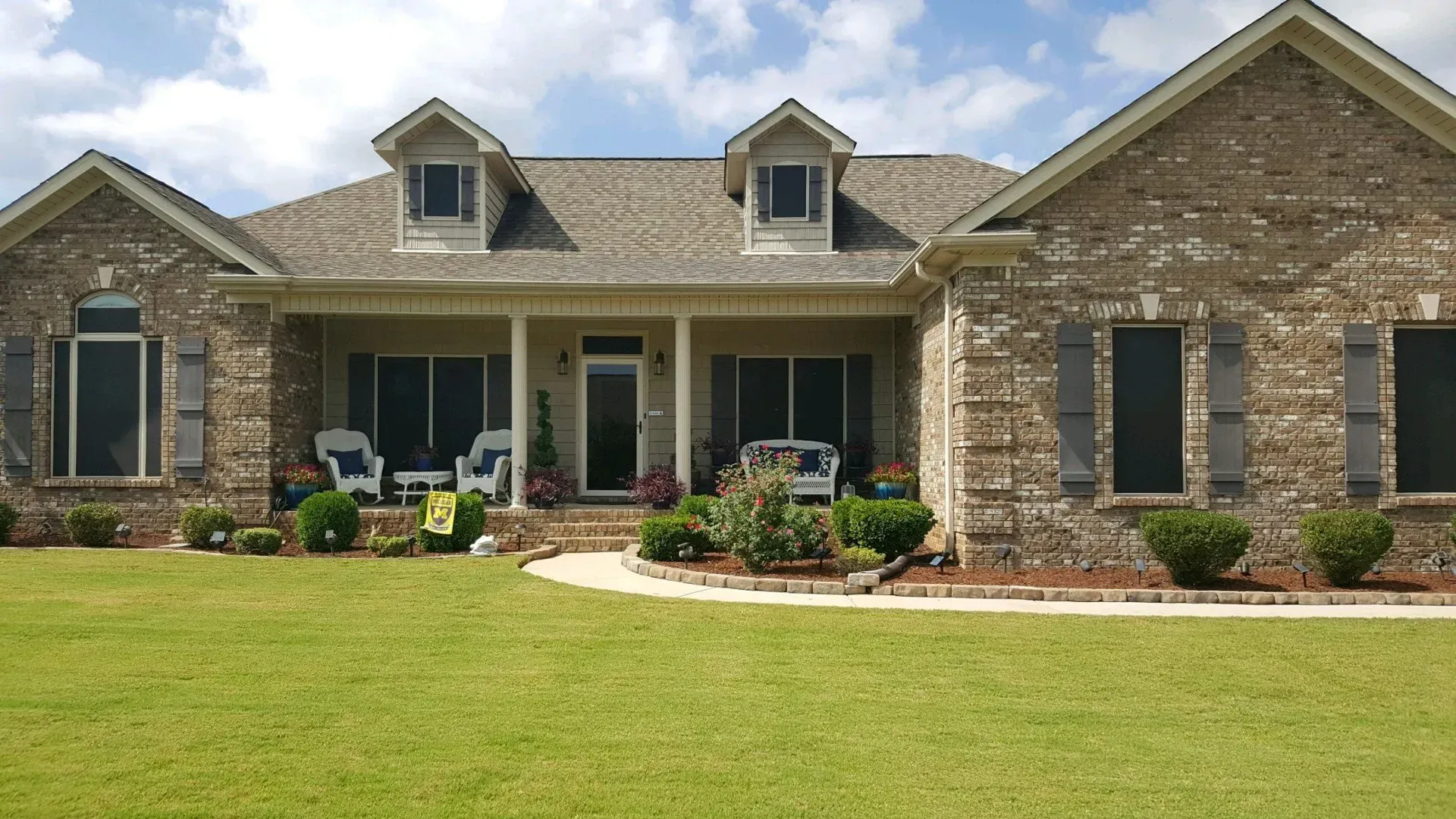 Single-story brick house with a front porch, black shutters, and a green lawn