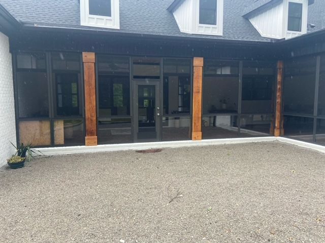 Front view of a house with dark siding, wood posts, and a gravel driveway under a covered porch
