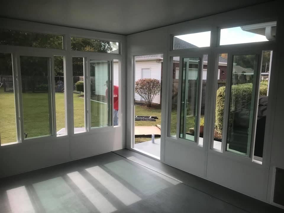 Empty sunroom with white-framed glass doors and windows, sunlight casting long shadows on the floor.