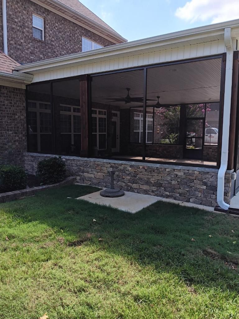 Screened back patio beside a brick house with a grassy yard and a small stone fountain.