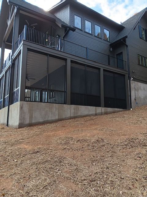 Large dark-gray house with covered porches on a sloped dirt lot