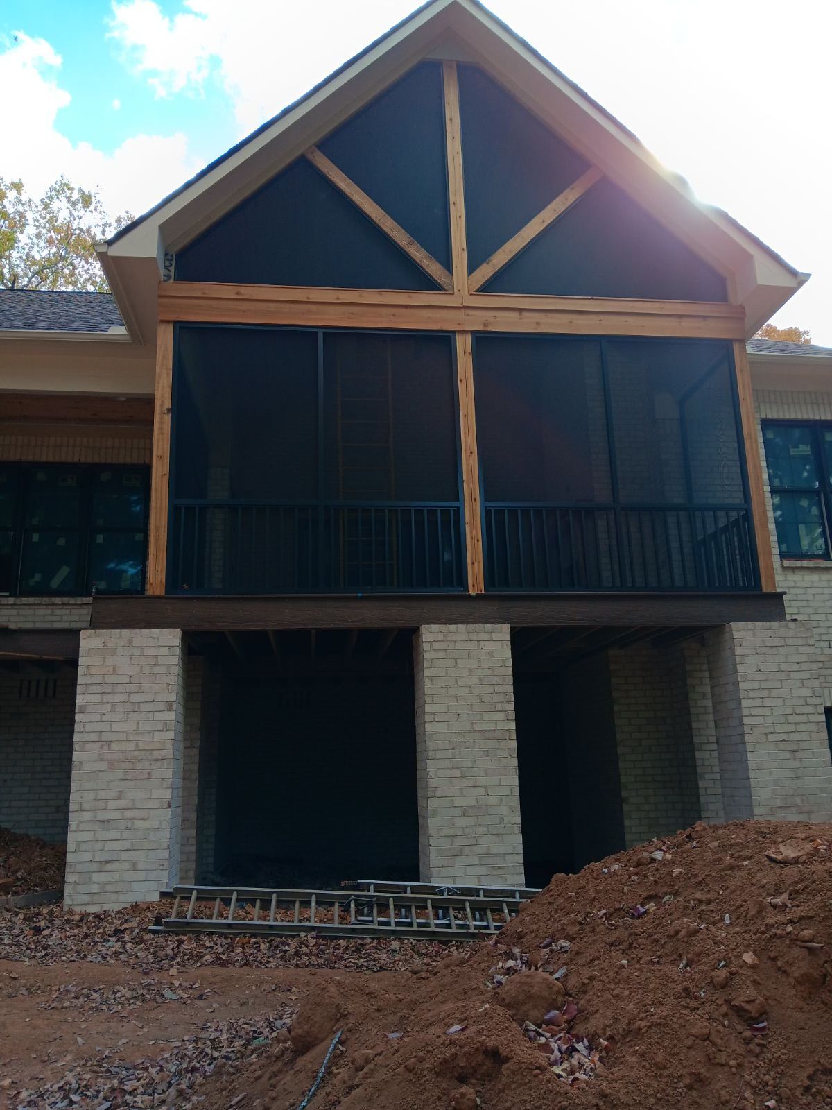 Two-story house with a screened porch, stone columns, and a dirt foreground under construction