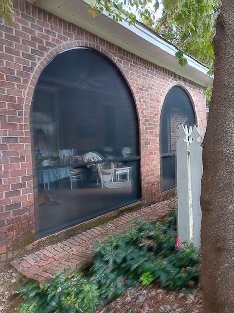 Brick house with large arched screened windows, brick planter, and white garden statue in front.