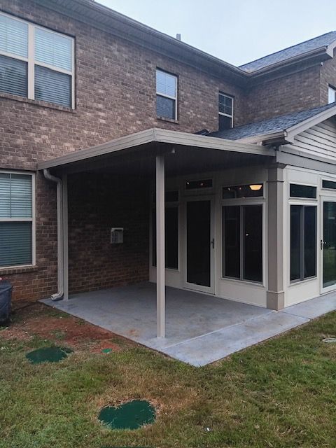 Brick house back patio with covered porch, concrete slab, and screened sunroom.