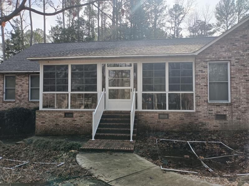 Front view of a brick house with screened porch, white steps, and bare trees in front