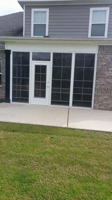 Patio doors and windows on the back of a gray house, with a concrete patio and green lawn.