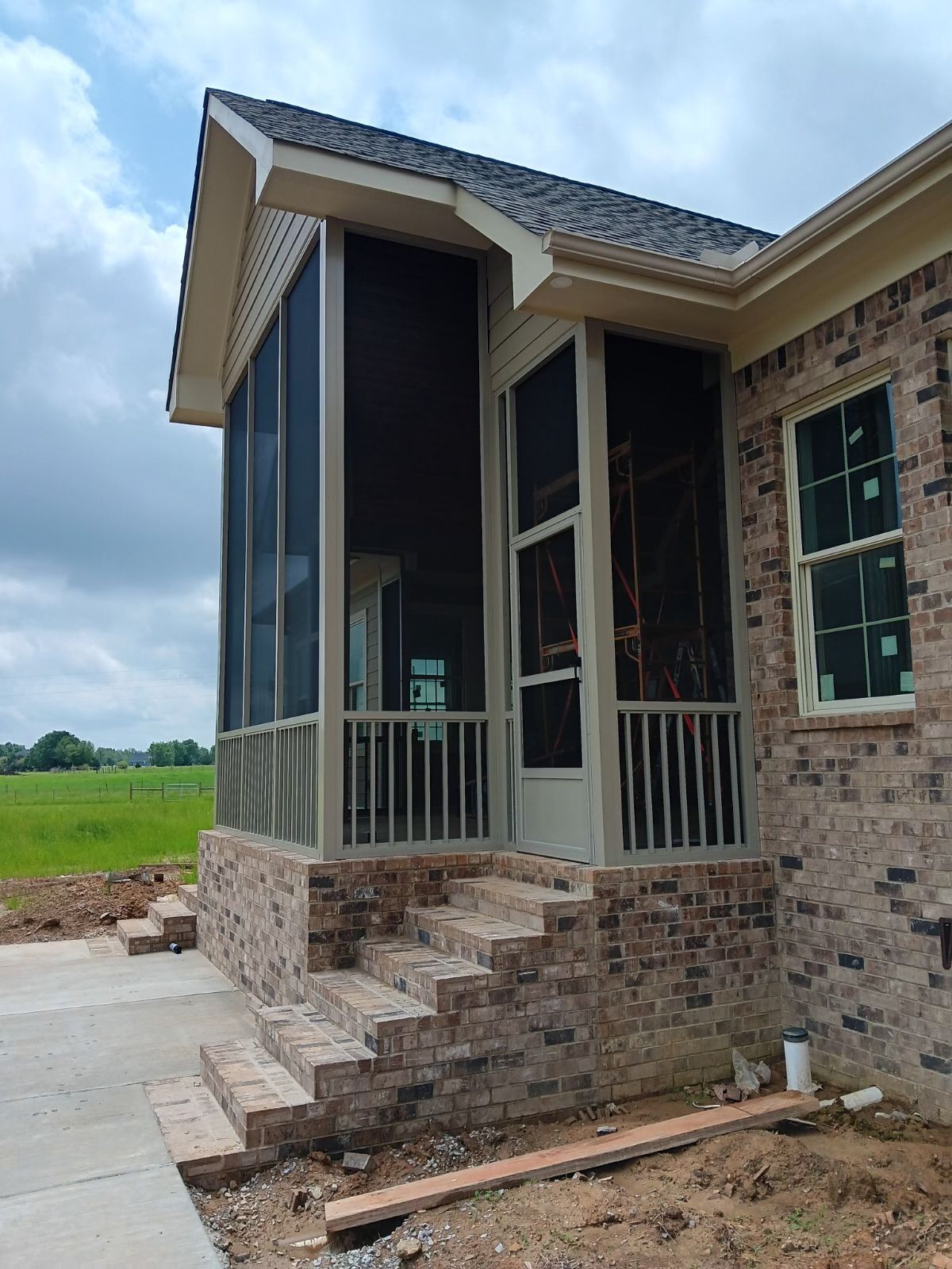 Brick house front porch with screened entry, steps, and cloudy sky over open field