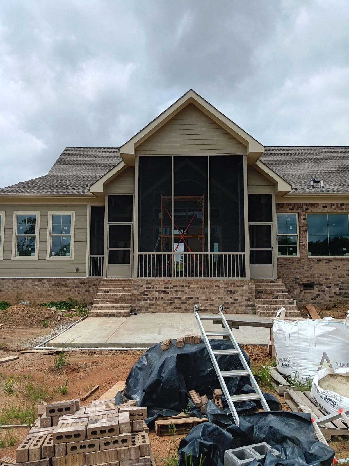 Partially built house with porch, ladders, and construction materials in the front yard under cloudy skies