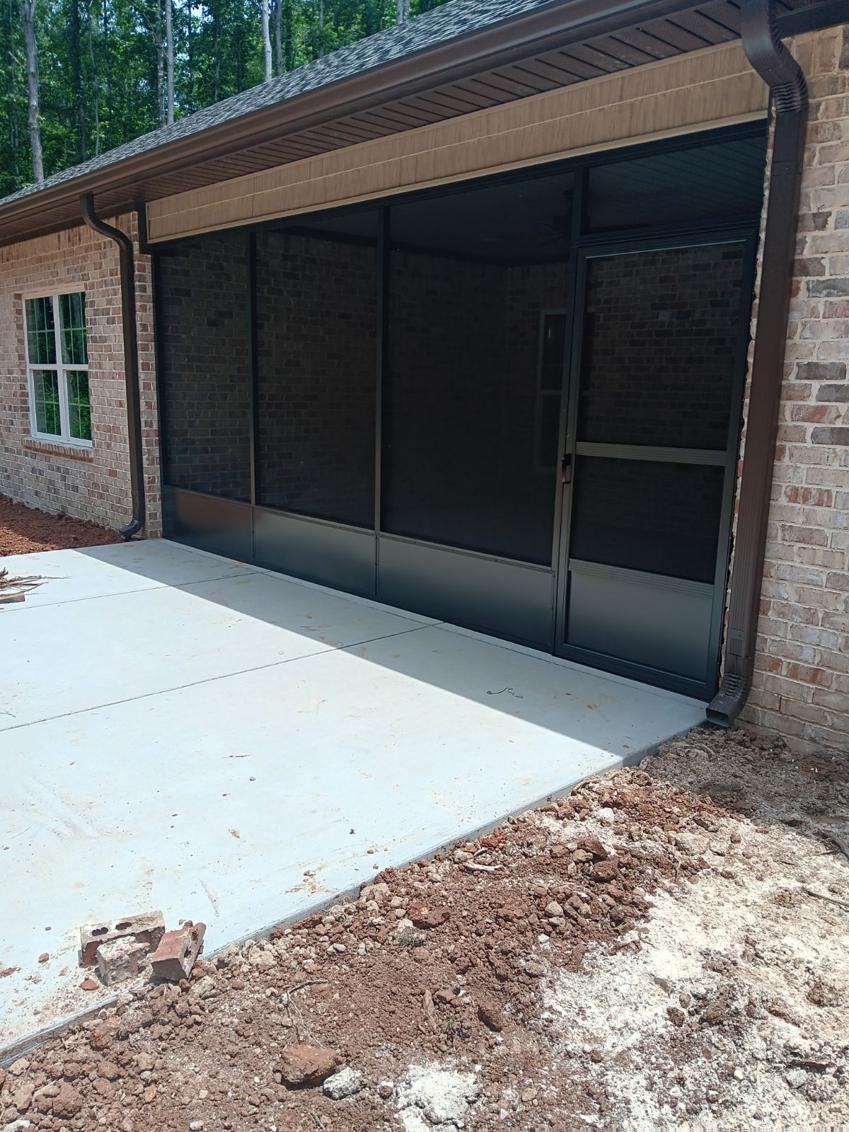Brick house patio with a screened-in porch and concrete slab under a sloped roof.