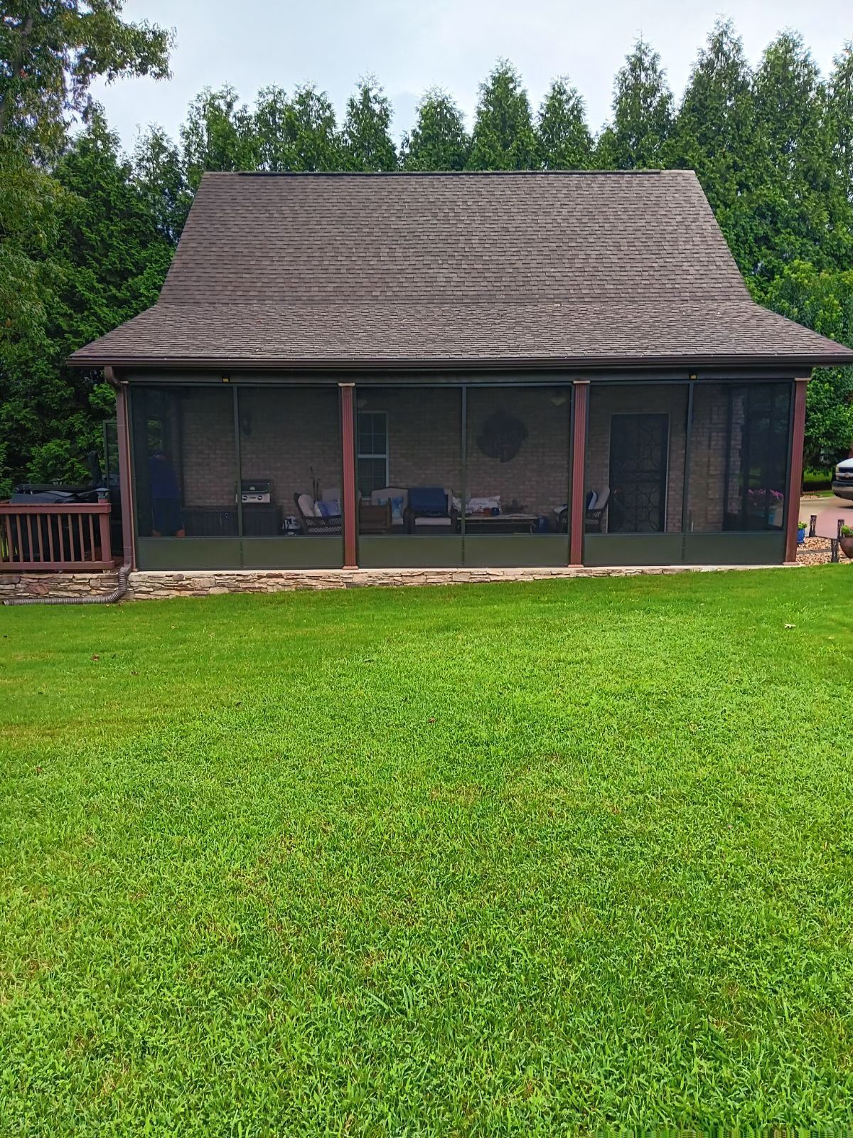 Small rustic pavilion with a shingled roof beside a green lawn and trees.