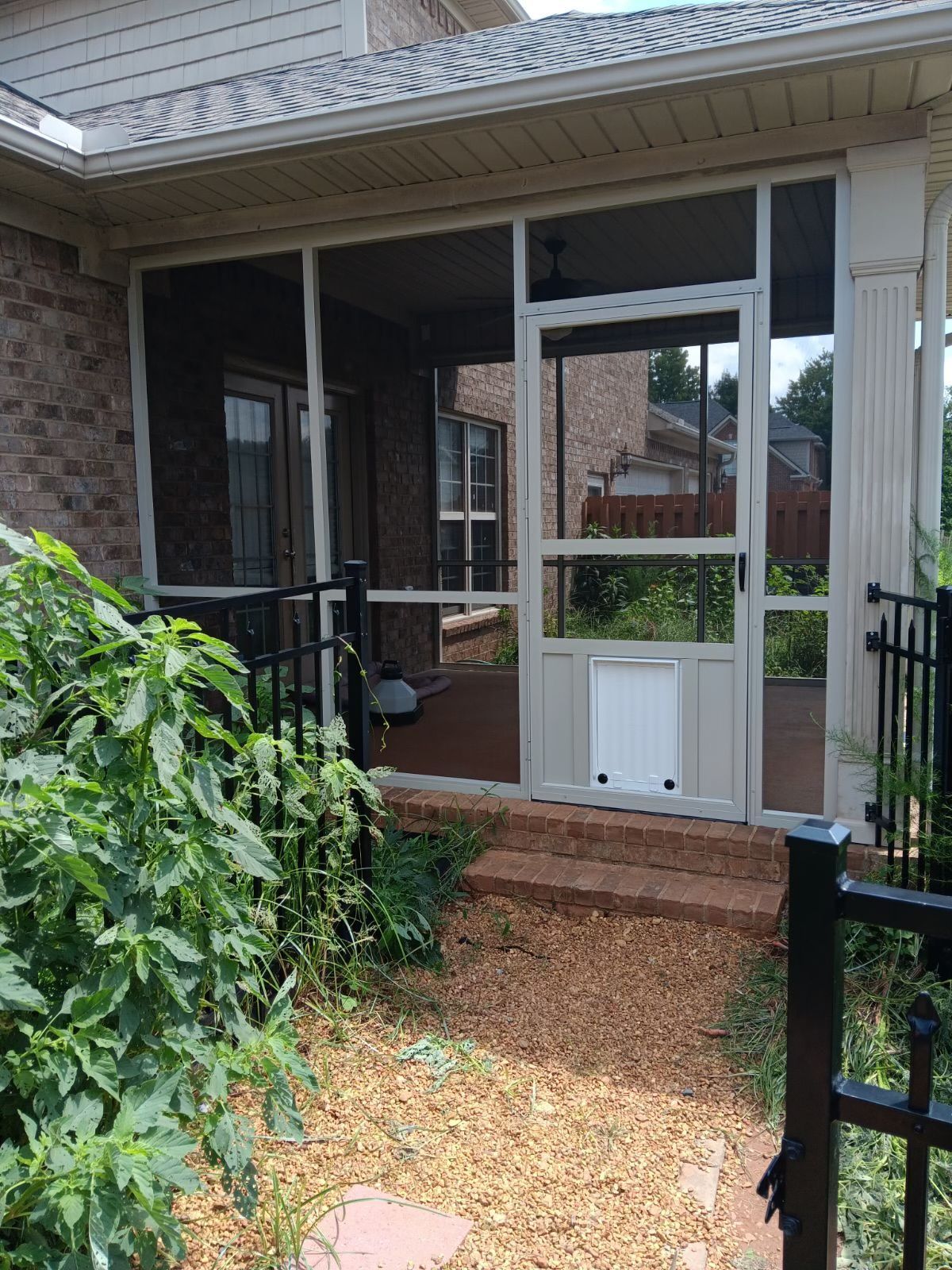 Brick house screened porch with white railings and a small white pet door over a gravel path.