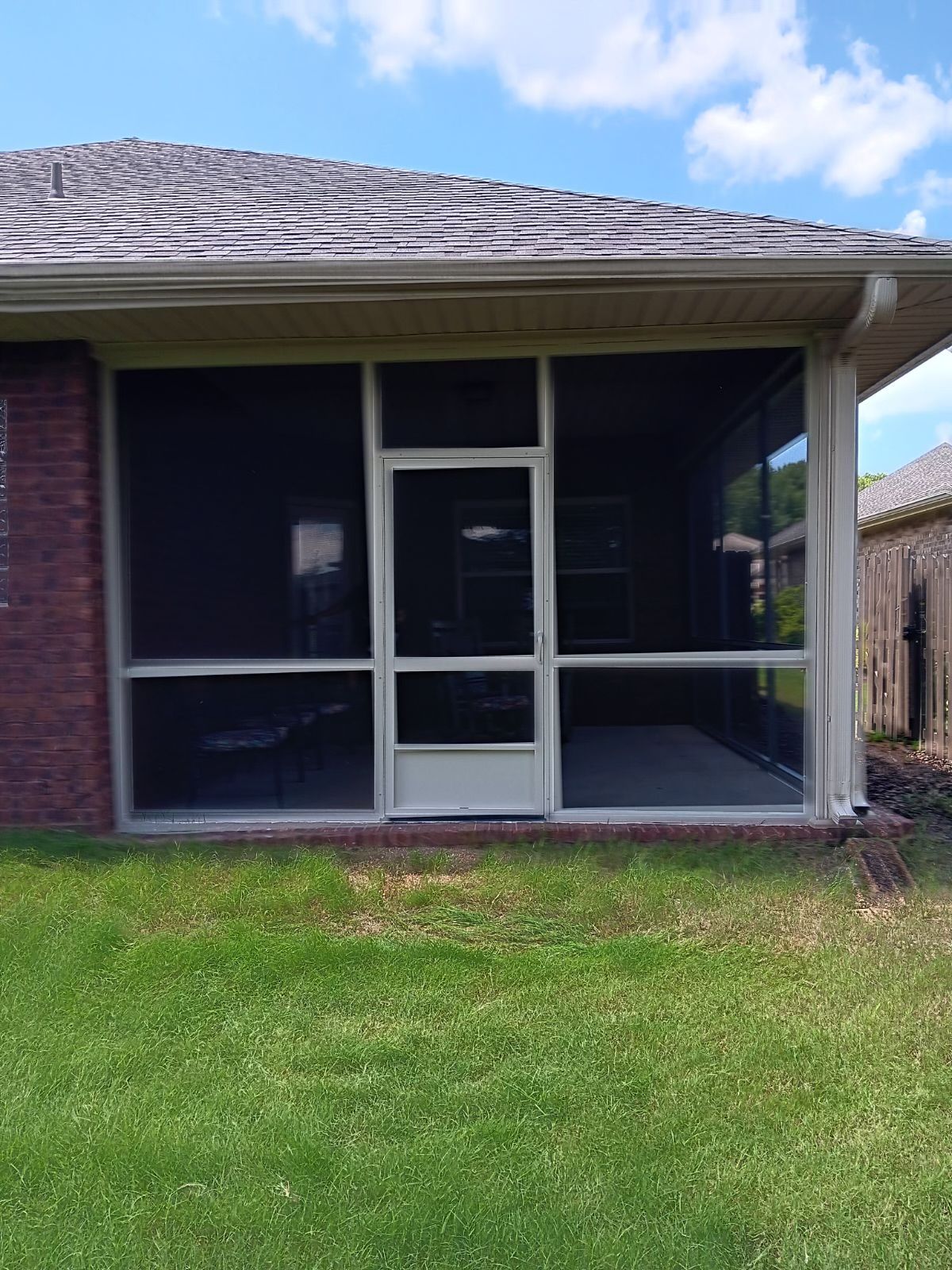 House porch with screened enclosure, white door, and green lawn under a cloudy sky