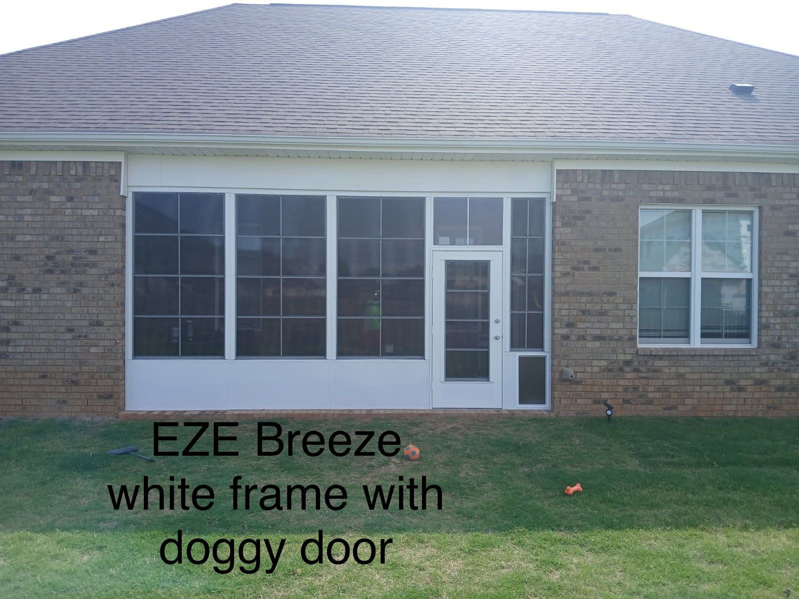 Brick house rear patio enclosure with white frame and doggy door beside a grass lawn