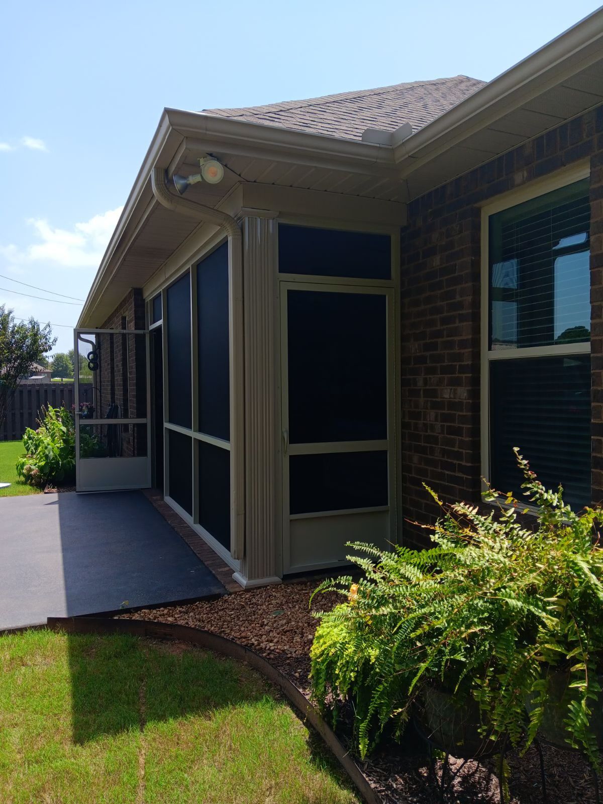 Side view of a brick house with screened patio, concrete walkway, and green lawn.
