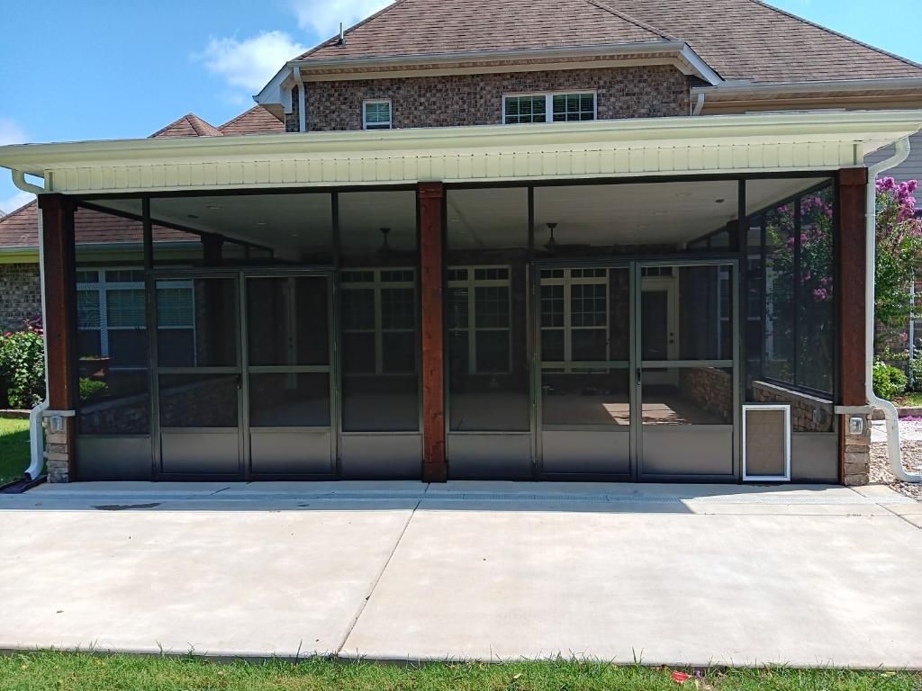 Covered building entrance with glass doors, brown columns, and a concrete driveway in front.