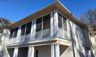 Two-story beige house with screened porch and white railings under a blue sky