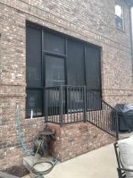 Brick apartment exterior with dark window bars and a small patio area with a hose and grill cover