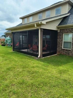Backyard screened porch attached to a beige house with brick lower siding and green lawn