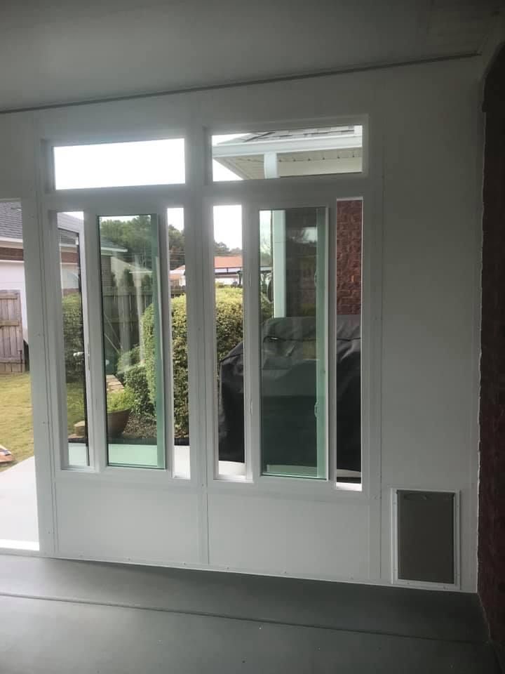 White patio doors with vertical blinds, leading to a backyard garden.