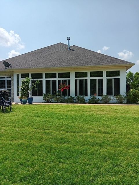 Single-story house with a gray roof, white trim, and a large green lawn under a blue sky
