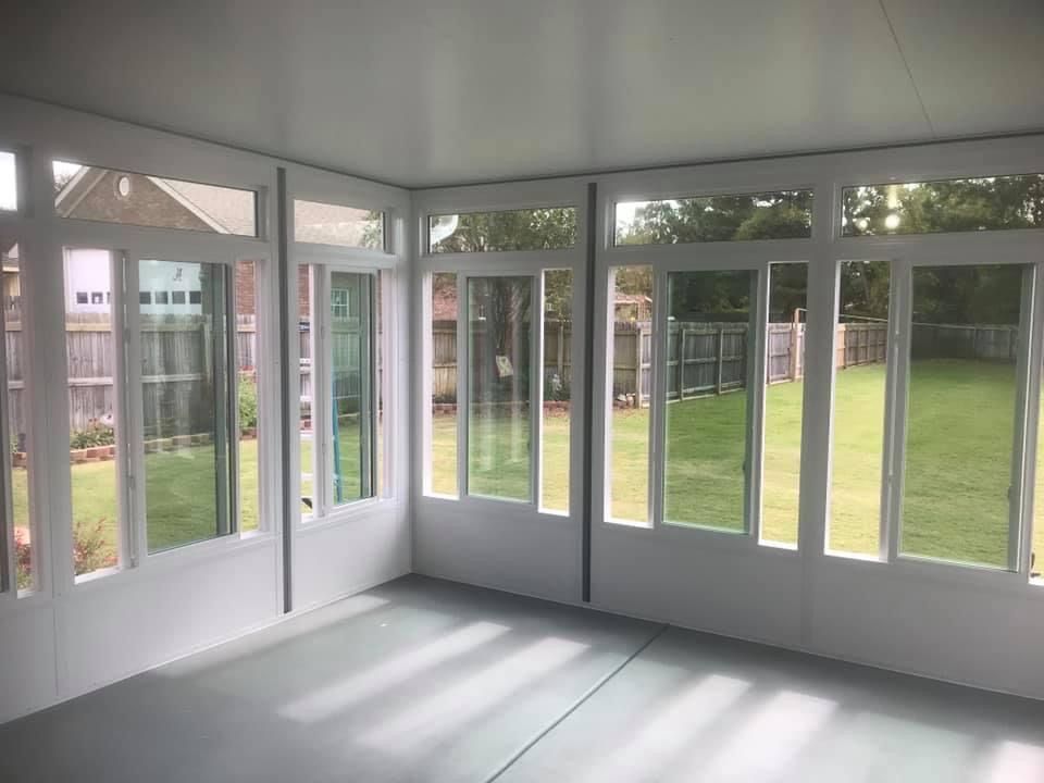 Bright sunroom with white framed windows and doors overlooking a green backyard.
