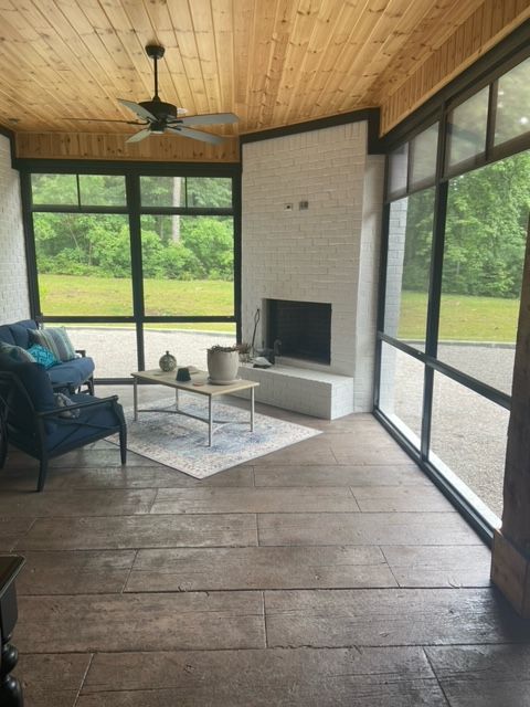 Screened porch with wood ceiling, large windows, fireplace, teal chair, and a small coffee table on a rug.