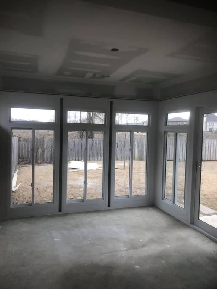 Empty unfinished sunroom with large windows, gray walls, and a concrete floor.
