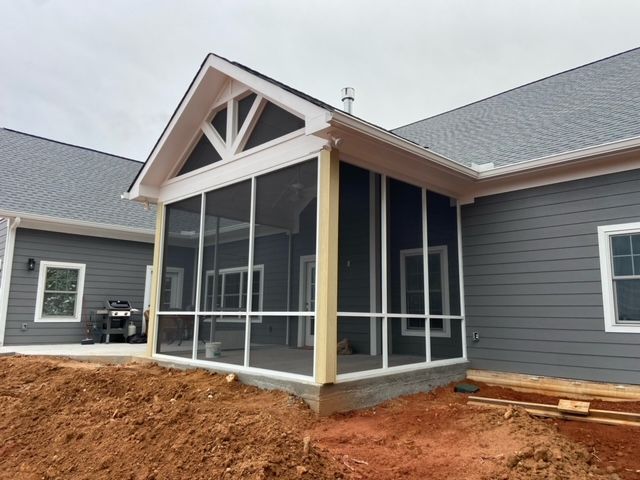 Enclosed front porch addition with screened windows and gray siding on a house under construction