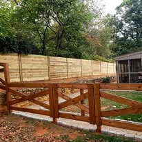 Wooden fence in a yard with a gate, trees in the background.