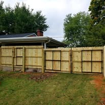 Wooden fence with multiple gates, adjacent to a home's exterior, in a grassy yard.