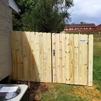 Wooden fence gate, natural wood color, in a yard next to a building.