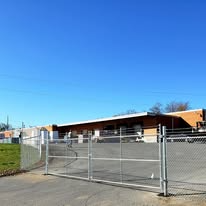 Metal gate in front of a long, low, brick building. Bright, cloudless, blue sky.