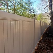 Beige vinyl fence runs along a wooded area.