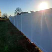 White vinyl fence in a grassy yard under a bright sun.