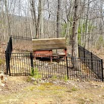 Black fenced enclosure with a weathered wooden structure in a forest setting.
