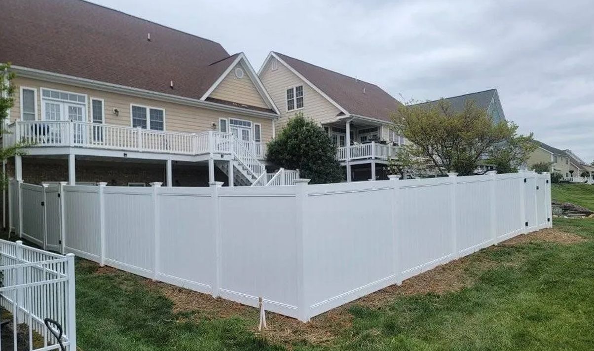 White vinyl fence surrounds a house with a deck on a cloudy day.