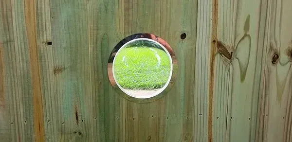 A circular hole cut into a wooden fence, revealing green grass.