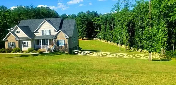 A large house with a green lawn and a white fence, surrounded by trees under a blue sky.