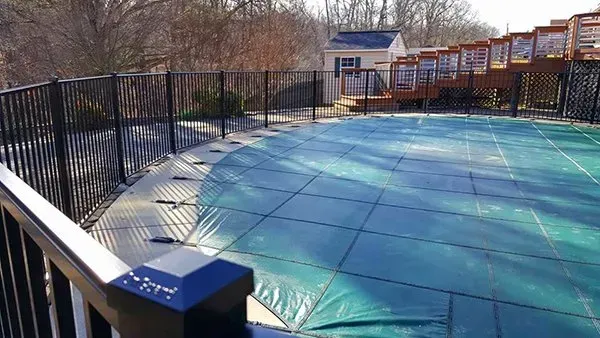 Pool covered with a green tarp, surrounded by a black fence and a wooden deck.