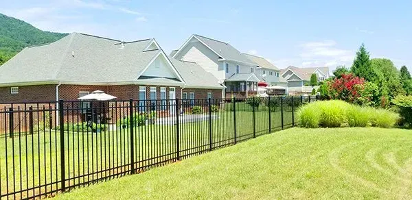 Black fence in front of a green lawn and houses. Mountains and trees in the background under a blue sky.