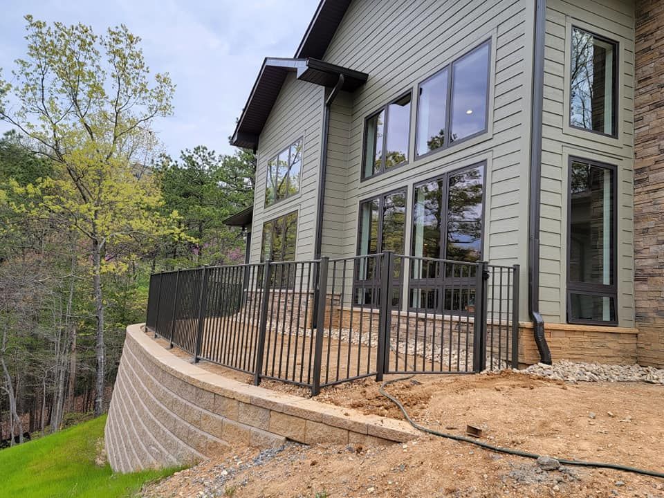 Exterior view of a house with black railing, large windows, and retaining wall.