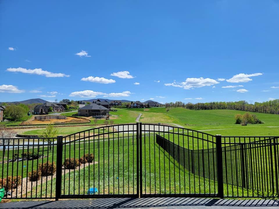 Black metal fence overlooking a green hillside dotted with houses under a blue sky with clouds.